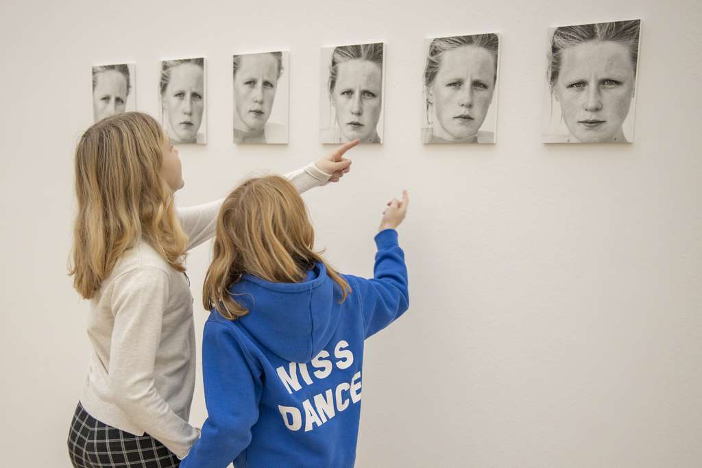 Deux personnes regardent les portraits d'une femme dans le mur.