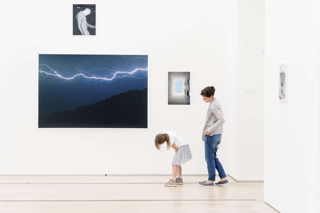 A woman and a young girl in front of a collection of fotos in an exhibition room.