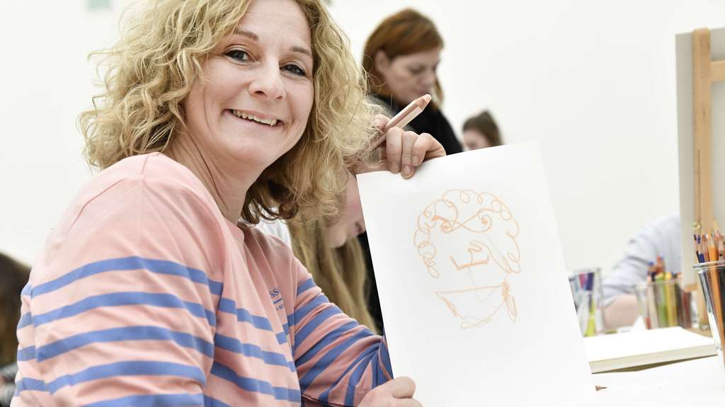 Lächelnde Frau schaut ins Kamera mit einer Zeichnung in der Hand.