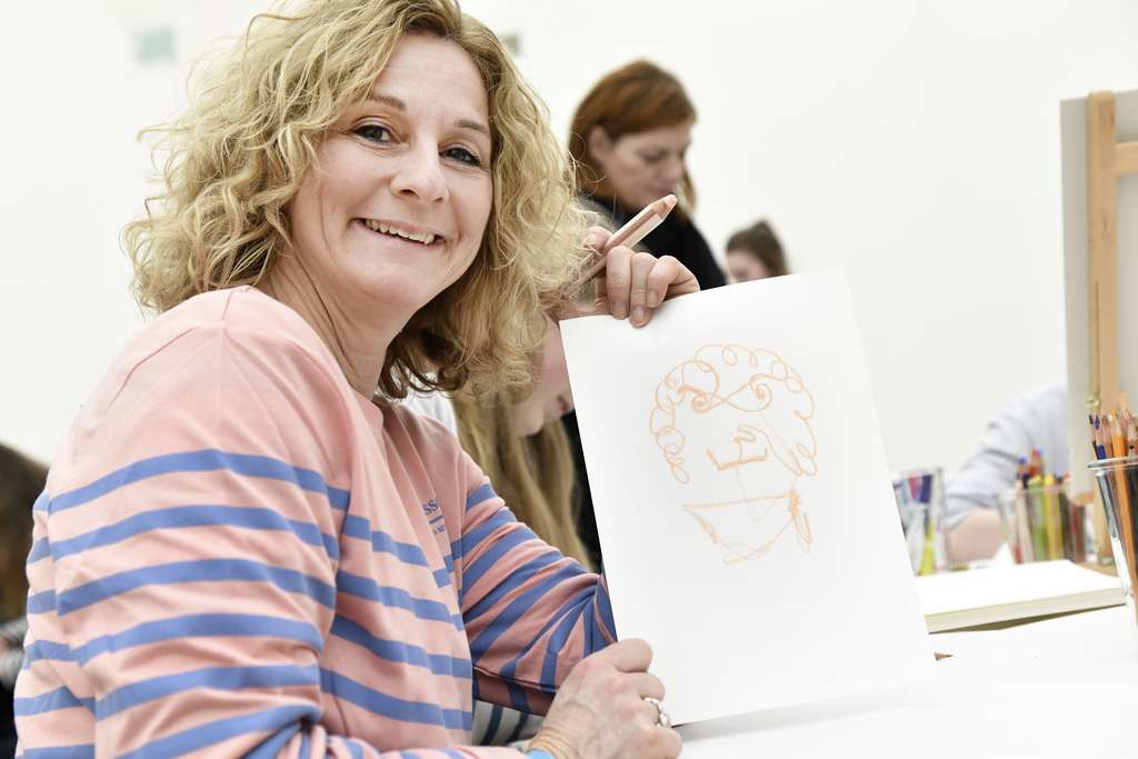 Smiling woman looks into the camera while holding a drawing in her hand.