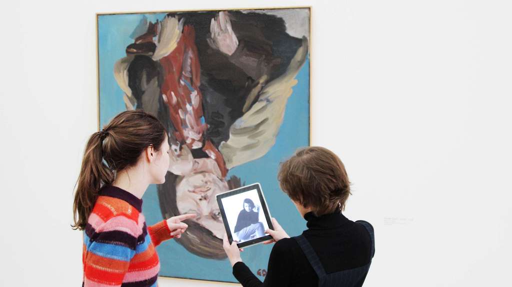 Visitors stand in front of a modern portait with a tablet in their hand.
