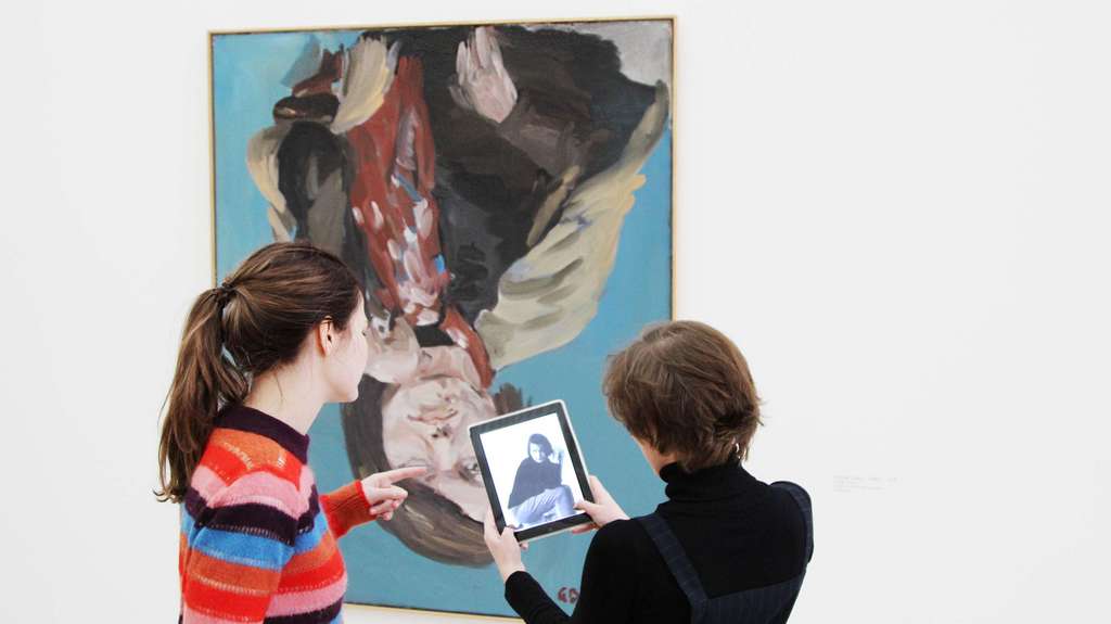 Besuchende stehen mit Tablet in der Hand vor einem zeutgenössischen Porträt.