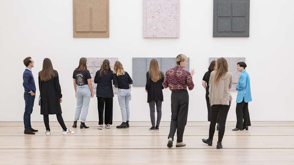 Young people in exhibition room look at art filled wall