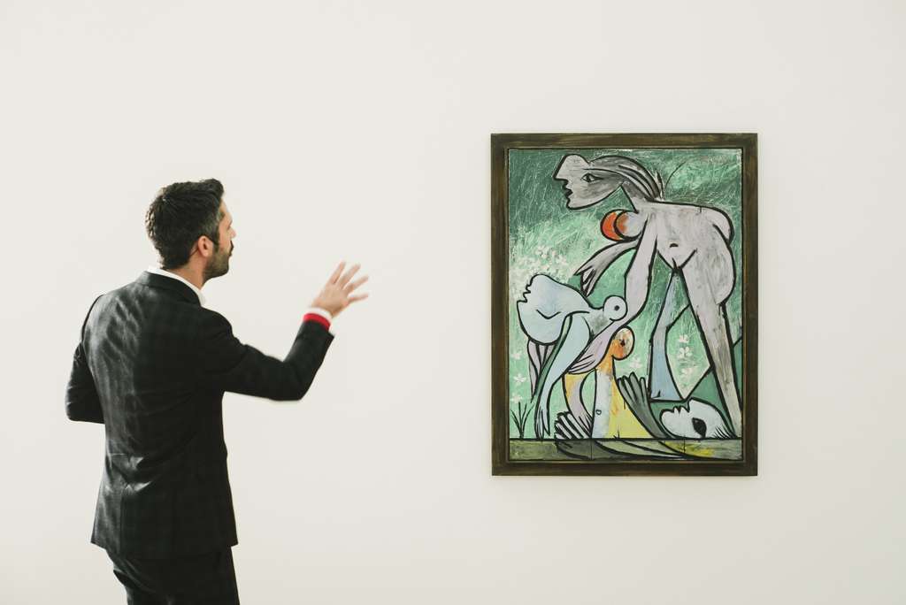 Curator R. Bouvier presents a painting in a museum hall.