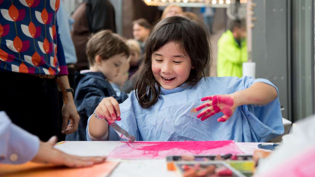 Ein glückliches Mädchen arbeitet mit pinker Fabe in einem Workshop im Museum.