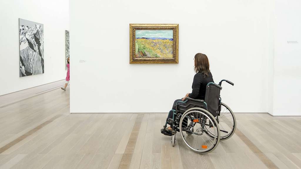 Personne en fauteuil roulant regardant un tableau représentant un paysage.