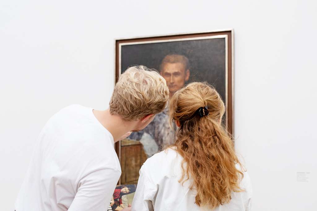 Zwei Menschen schauen ein Porträt an der Wand an.