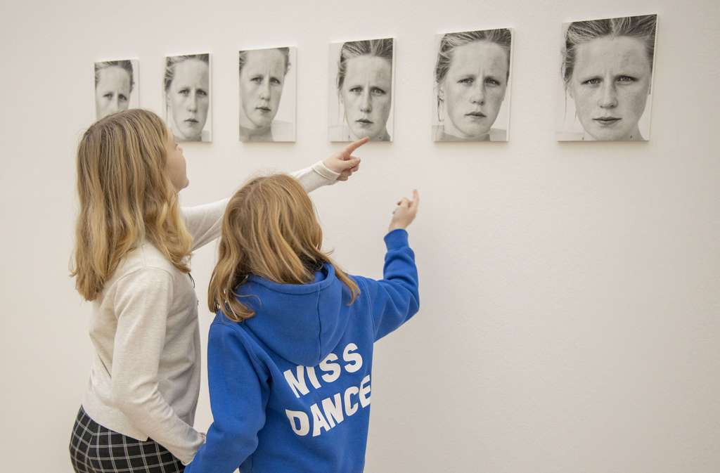 Two people look at portaits of a woman in the wall.