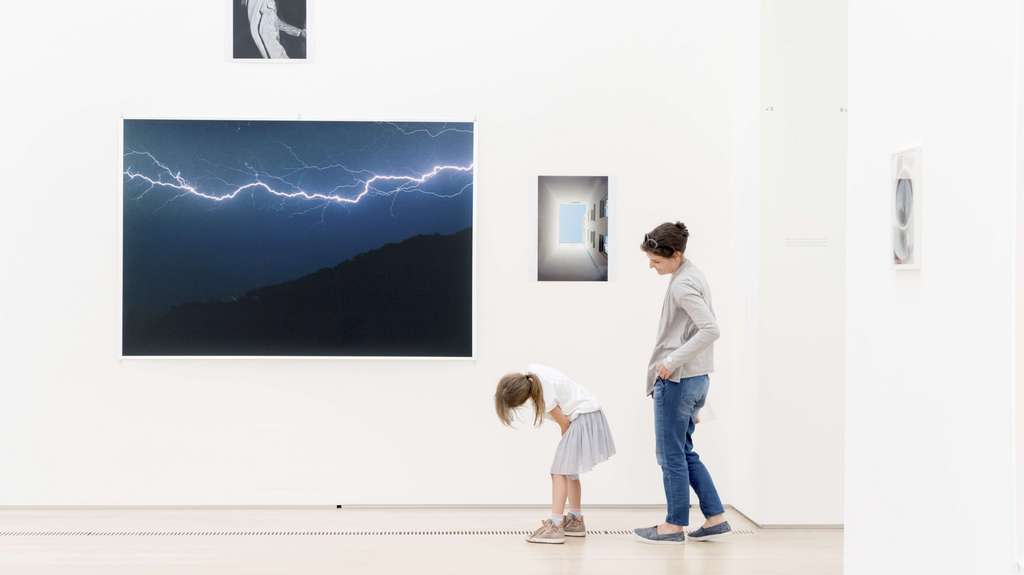 Une femme et une jeune fille devant une collection de photos dans une salle d'exposition.