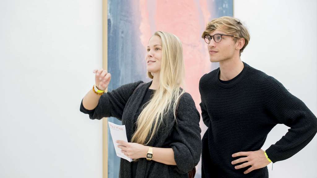 Deux jeunes gens se tiennent devant un tableau et parlent d'art.