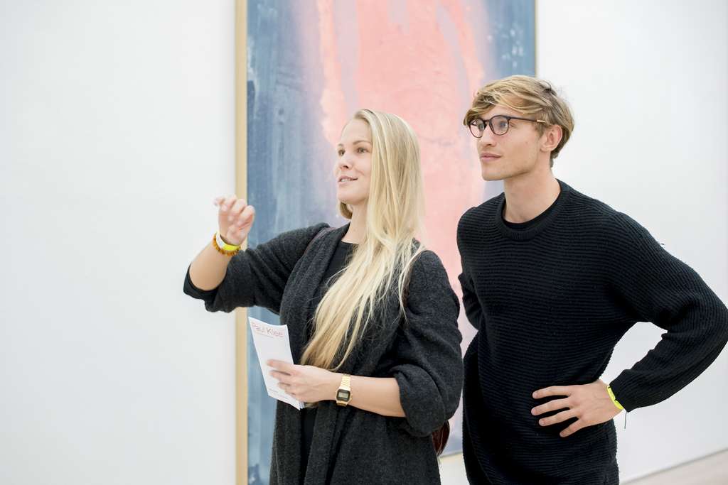 Two young people stand in front of a painting and talk about art.