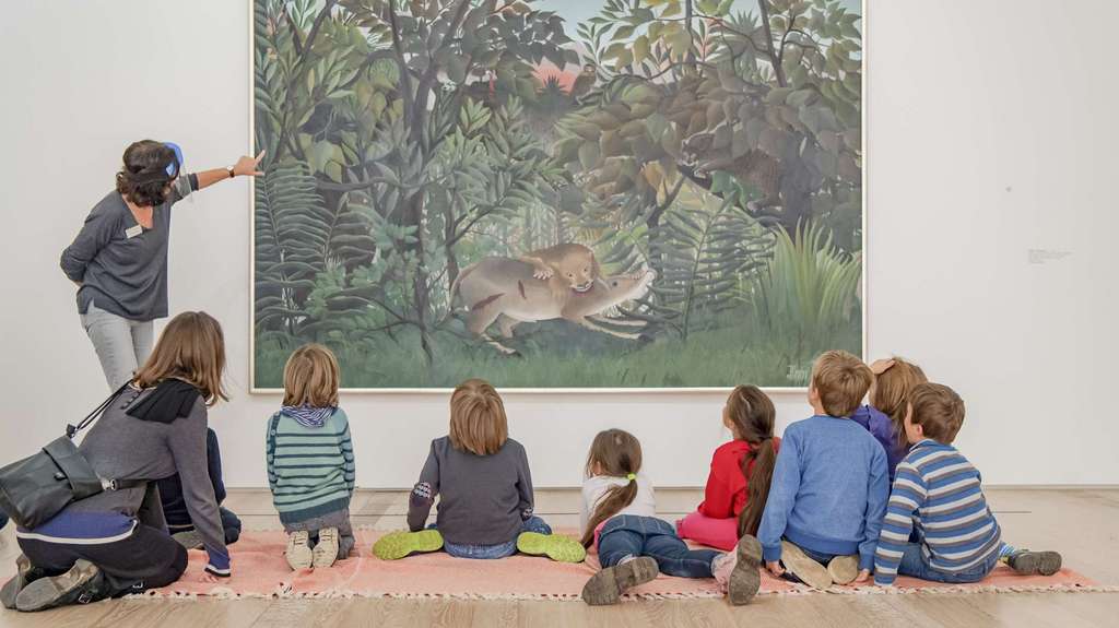Eine Frau stellt eine Kindergruppe ein Kunstwerk von Rousseau vor.
